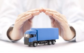Car insurance. Blue truck miniature covered by hands.